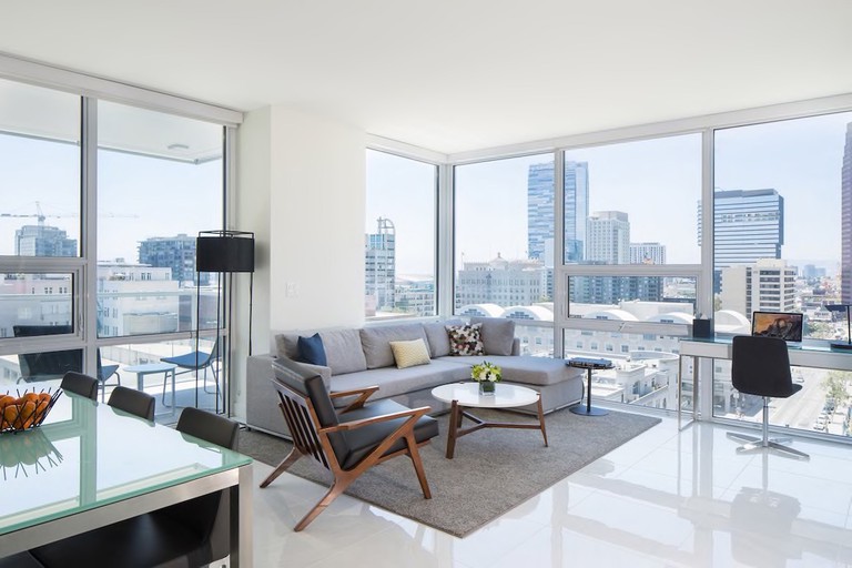 Corner apartment with shiny white floors, grey couch and floor-to-ceiling wraparound windows with city views at LEVEL Los Angeles
