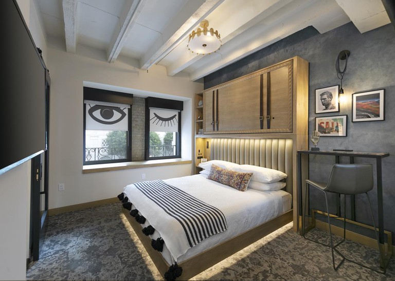 Hip guest room with under-bed lighting, blinds painted with winking eyes and framed prints at the Wayfarer Downtown LA