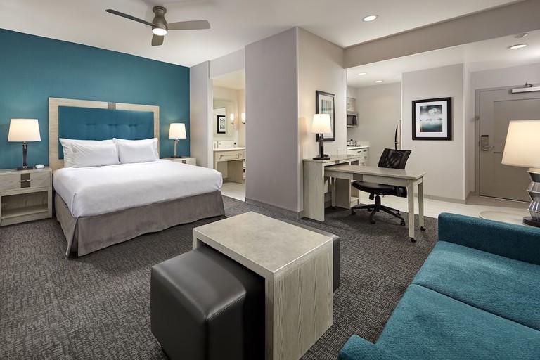 Spacious king suite in grey and peacock-blue hues with kitchen, desk and couch at Homewood Suites by Hilton Long Beach Airport