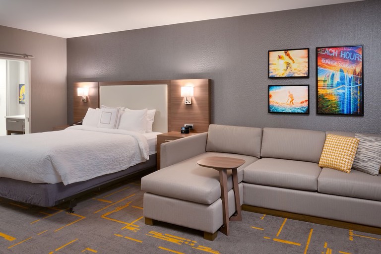 Suite with L-shaped couch, surfer-themed art and patterned carpet at TownePlace Suites by Marriott Los Angeles LAX/Hawthorne